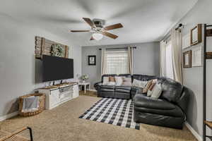 Carpeted living area with a ceiling fan and baseboards
