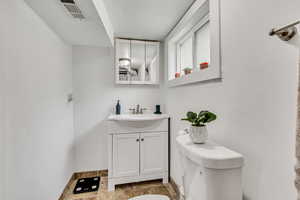Half bath featuring stone tile flooring, vanity, toilet, and baseboards