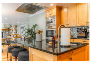 Kitchen featuring crown molding, light brown cabinetry, stainless steel appliances, backsplash, and under cabinet range hood