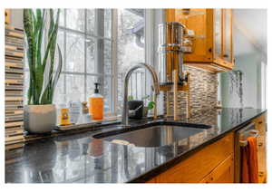 Kitchen with a sink, brown cabinetry, dark stone countertops, tasteful backsplash, and glass insert cabinets