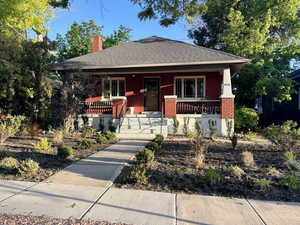 Bungalow-style house with brick siding, roof with shingles, covered porch, and a chimney