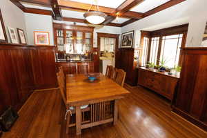 Dining area featuring a wainscoted wall, beamed ceiling, coffered ceiling, and dark wood-type flooring