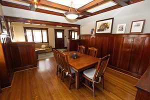 Dining area featuring coffered ceiling, beam ceiling, dark wood-style floors, and wainscoting