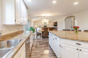 Kitchen featuring arched walkways, light wood-style flooring, ceiling fan, a sink, and lofted ceiling