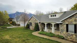 View of front of property with a porch, a front yard, a shingled roof, a mountain view, and stone siding