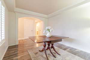 Dining area featuring baseboards, arched walkways, wood finished floors, and crown molding