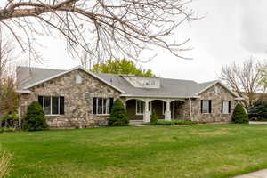 Ranch-style home with a porch, a shingled roof, a front lawn, and stone siding
