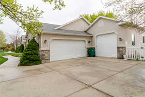 Exterior space featuring an attached garage, concrete driveway, stone siding, and stucco siding