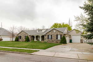 View of front facade with a garage, concrete driveway, a front yard, and stone siding