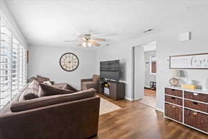 Living room featuring visible vents, dark wood-style flooring, baseboards, ceiling fan, and a textured ceiling