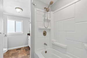 Full bathroom with visible vents, toilet, baseboards, stone finish flooring, and shower / washtub combination