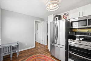 Kitchen with baseboards, white cabinets, stainless steel appliances, and dark wood-style flooring