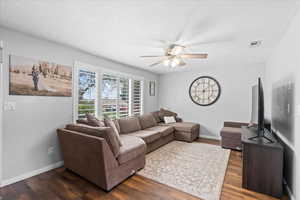 Living room with baseboards, ceiling fan, dark wood finished floors, and visible vents
