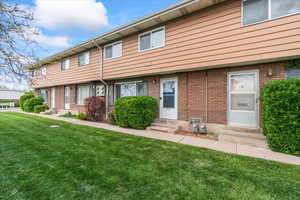 Townhome / multi-family property featuring brick siding, a front lawn, and entry steps