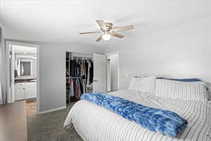 Carpeted bedroom with a closet, baseboards, ensuite bathroom, and ceiling fan