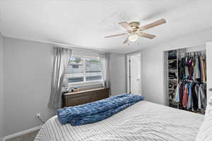 Carpeted bedroom featuring a textured ceiling, baseboards, ceiling fan, and a closet