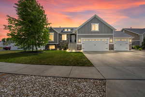 Craftsman inspired home with board and batten siding, a yard, an attached garage, concrete driveway, and stone siding