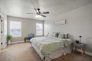 Carpeted Primary bedroom with a textured ceiling, baseboards, and ceiling fan