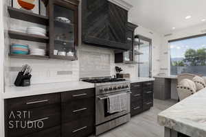 Kitchen featuring light countertops, glass insert cabinets, tasteful backsplash tiled to the ceiling, and high end stainless steel range oven