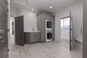 Laundry with stacked washer and dryer, a sink, gray cabinets, light wood look tile floors