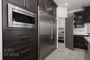 Kitchen with light countertops, built in appliances, tasteful backsplash, and dark brown cabinetry