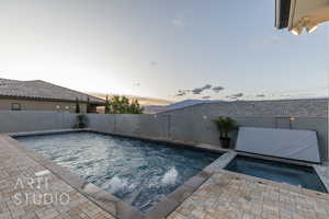 Pool at dusk with a fenced in pool, a fenced backyard, an in ground hot tub, and a patio area
