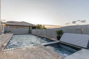 Pool at dusk featuring a fenced in pool, a fenced backyard, an in ground hot tub, and a patio