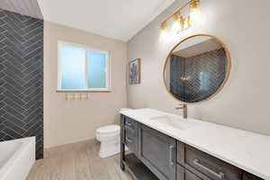 Bathroom featuring vanity, baseboards, a bathing tub, and toilet