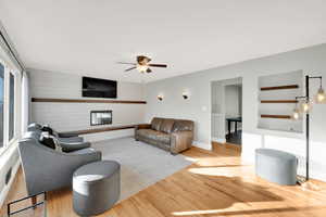 Living room with wooden walls, ceiling fan, a large fireplace, baseboards, and wood finished floors