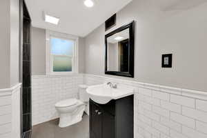 Bathroom featuring vanity, toilet, tile walls, and a wainscoted wall