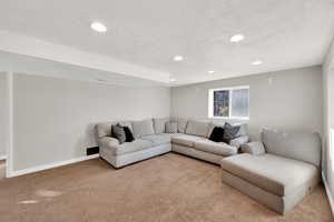 Carpeted living room with recessed lighting, a textured ceiling, and baseboards