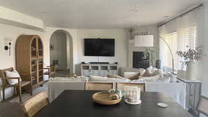 Carpeted living area featuring arched walkways, a textured ceiling, and visible vents