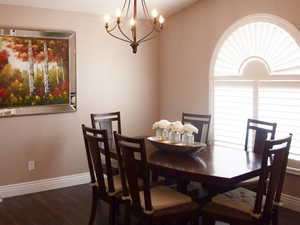 Dining area with baseboards, vaulted ceiling, dark wood-type flooring, and a notable chandelier