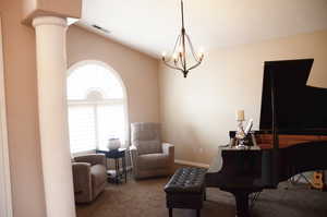 Carpeted living room with vaulted ceiling, ornate columns, a chandelier, and visible vents