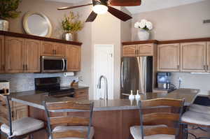 Kitchen featuring a kitchen breakfast bar, a ceiling fan, backsplash, appliances with stainless steel finishes, and a sink