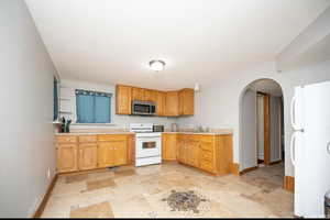 Kitchen featuring stone finish floor, arched walkways, light countertops, baseboards, and white appliances