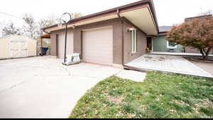 Exterior space with an attached garage, a storage unit, brick siding, and concrete driveway