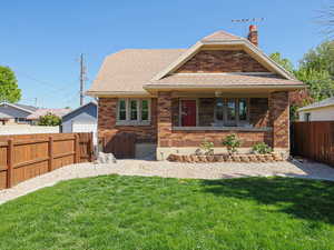 Back of house with brick siding, a fenced backyard, a lawn, and a chimney