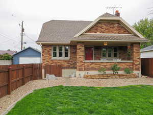 View of front facade featuring covered porch, a chimney, a front lawn, and brick siding