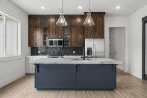 Kitchen with baseboards, an island with sink, tasteful backsplash, a sink, and appliances with stainless steel finishes