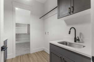 Clothes washing area with cabinet space, a sink, baseboards, hookup for a washing machine, and light wood-style floors