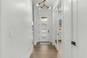 Doorway with light wood-type flooring, baseboards, and an inviting chandelier