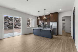 Kitchen with a breakfast bar area, dark brown cabinetry, baseboards, light wood-style floors, and stainless steel appliances