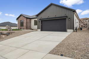View of front of property featuring board and batten siding, brick siding, an attached garage, and driveway