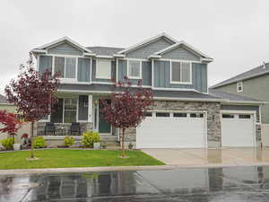Craftsman inspired home with a front lawn, stone siding, board and batten siding, a porch, and driveway
