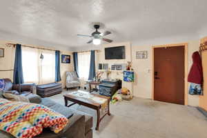 Carpeted living area featuring a ceiling fan and a textured ceiling