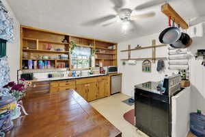 Kitchen featuring open shelves, light floors, ceiling fan, tile counters, and stainless steel appliances