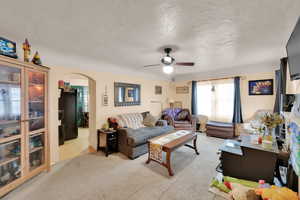 Living room featuring arched walkways, ceiling fan, light carpet, and a textured ceiling
