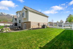View of property exterior featuring brick siding, a lawn, fence, and a mountain view