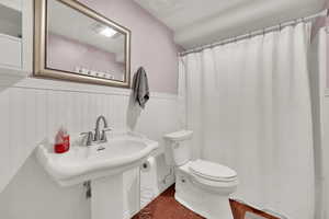 Full bath featuring a sink, toilet, a wainscoted wall, curtained shower, and wood finished floors